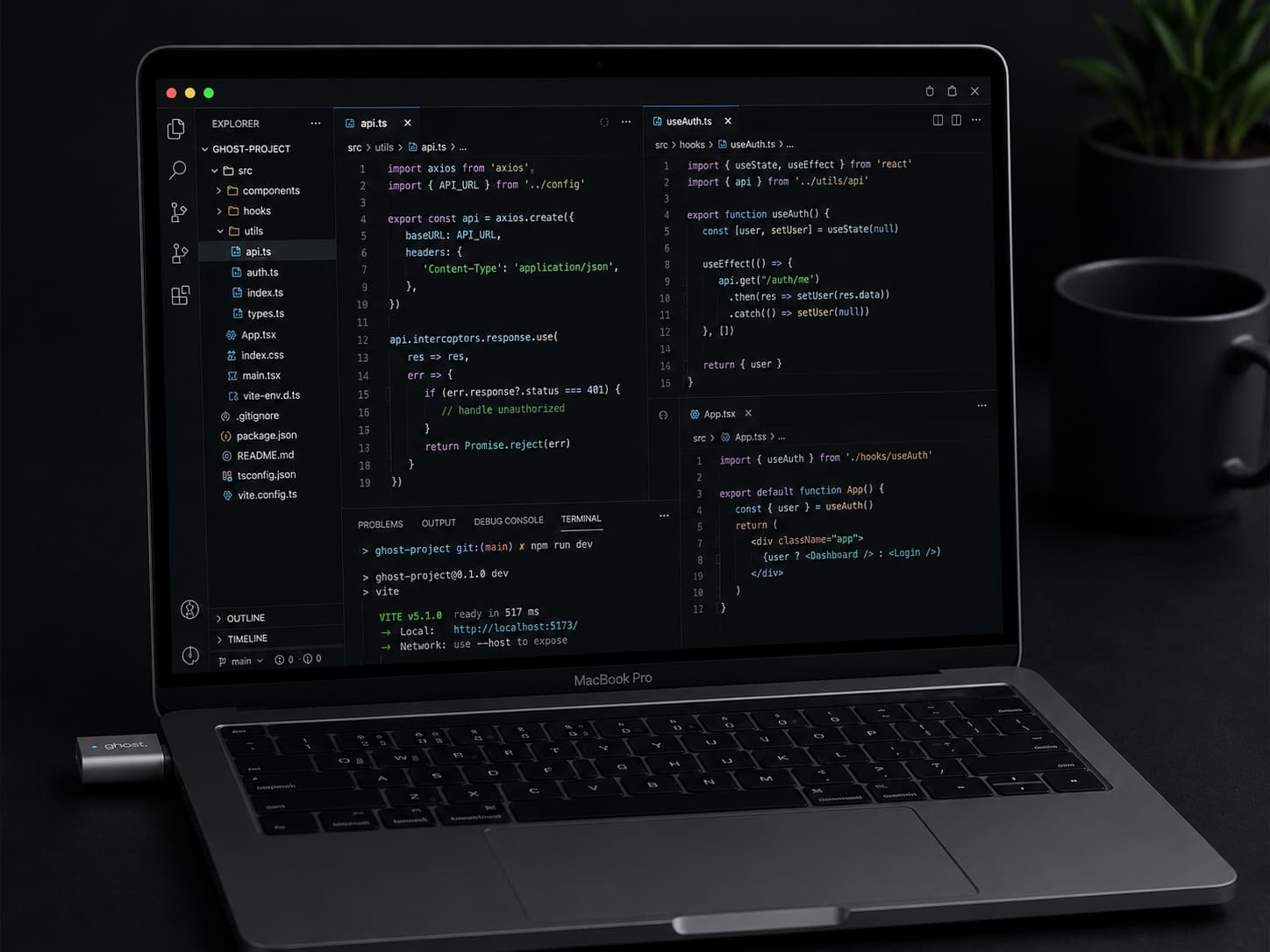 A MacBook on a dark desk running a Vite dev server in VS Code, with the Ghost dongle plugged into a side port.